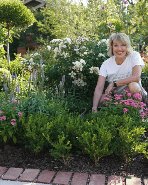 Smiling woman kneeling beside plantings of a boxwood border
